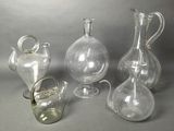 three clear glass vases and a glass pitcher on a gray background