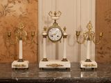 trois bougies et une horloge posées sur une table devant un mur
