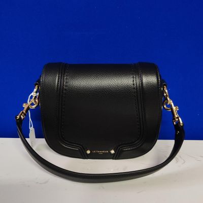 a black cross body bag on a white table with a blue background