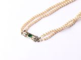 une photo d'un collier de perles blanches muni d'un fermoir orné d'une pierre verte