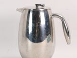 a silver pitcher with a handle on a white surface
