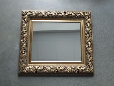 miroir à cadre doré posé au sol, avec un mur blanc en arrière-plan