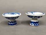 une paire de bols en porcelaine bleue et blanche posés sur des socles, sur une table