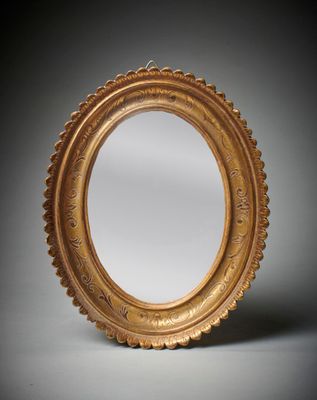un miroir ovale avec un cadre doré sur fond gris