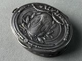 an antique silver box with a bird on it sitting on top of a table