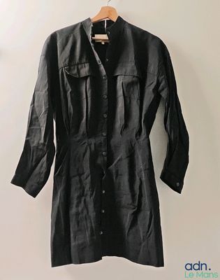 une robe-chemise noire suspendue à un cintre devant un mur blanc