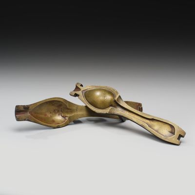 une paire de cuillères en bronze et un repose-cuillère posés sur une surface blanche