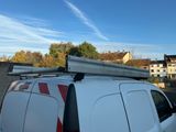 une camionnette blanche garée sur un parking, avec une échelle posée sur le toit