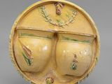 une image représentant un vase jaune orné de deux gros seins