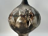 a black vase with a design on it sitting on a white surface