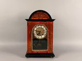 a small red clock with a gold face on a white background