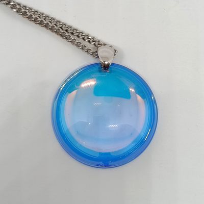 un pendentif en verre bleu muni d'une chaîne en argent, posé sur une surface blanche