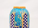 un vase bleu et jaune posé sur une surface blanche