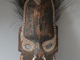 une image représentant un masque en bois orné de plumes sur fond blanc