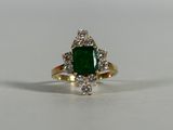 a close up of a ring with a green stone surrounded by diamonds