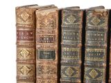 several old books are lined up in a row on a shelf