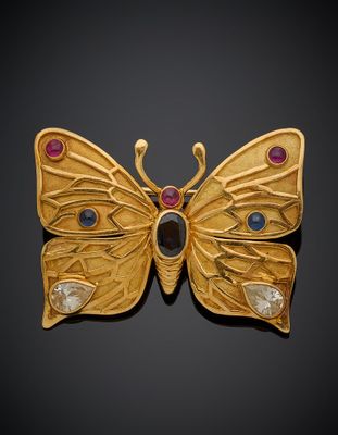 un gros plan sur une broche en forme de papillon en or ornée de pierres multicolores