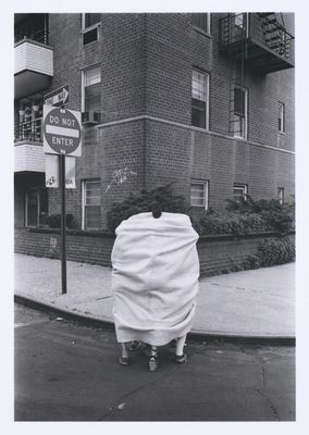 black and white photograph of a person wrapped in a blanket on a street corner