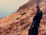an old photo of a woman standing on top of a hill next to a lake