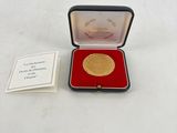 une photo d'une médaille d'or dans un écrin rouge, accompagnée d'un certificat