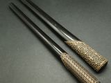 two black and gold handled chopsticks sitting on a black surface