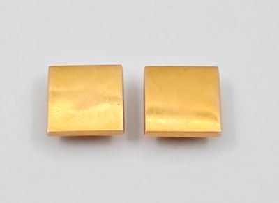 une paire de boucles d'oreilles carrées en or posées sur une surface blanche