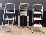 three metal ladders are lined up against a gray wall