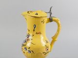 yellow pitcher with blue and yellow flowers on it sitting on a gray surface
