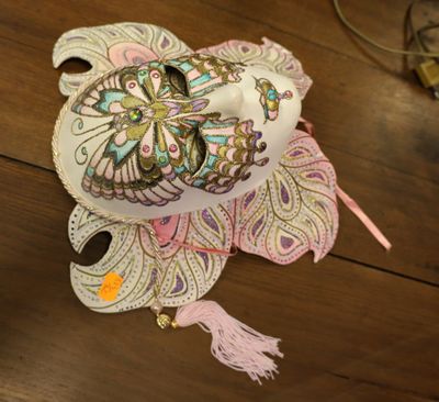 un masque blanc posé sur une table en bois, orné d'un pompon rose