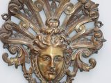 une plaque en or sur laquelle est représenté un visage, posée sur un fond blanc