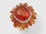 un gros plan d'une bague ornée d'une pierre orange entourée de pierres orange et blanches