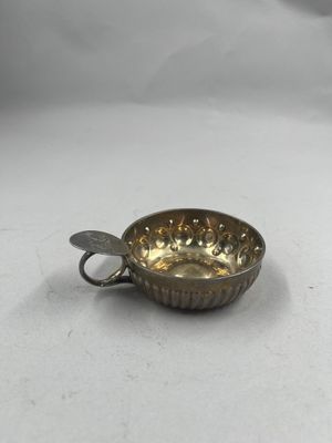 une petite tasse en argent contenant une cuillère, posée sur une surface blanche