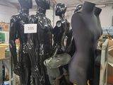 Plusieurs mannequins sont alignés sur un présentoir métallique dans un magasin.
