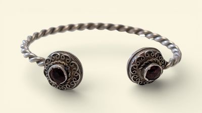 a close up of a silver bracelet with a red stone on it