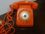 an orange telephone sitting on a wooden floor next to a wall