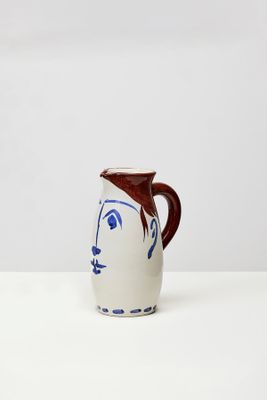 cruche en céramique blanche ornée d'un visage bleu et d'une anse marron sur fond blanc