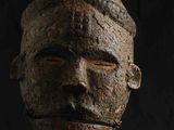 un gros plan d'un masque en bois posé sur un socle, sur fond noir