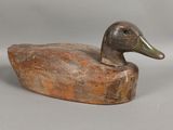 canard en bois sculpté, perché sur un morceau de bois, sur fond gris