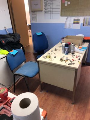 a room with a desk, chairs, a refrigerator, and a roll of toilet paper