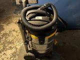 L'aspirateur est posé par terre à côté de la porte bleue.
