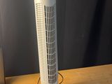 un ventilateur colonne blanc posé sur un bureau, à côté d'un ordinateur