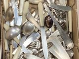 une boîte remplie de cuillères en argent et des cuillères posées par terre