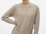 a woman wearing a beige sweater and black pants stands in front of a white background