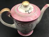 a pink teapot with a gold lid on a black table