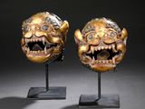 pair of carved masks on stands against a black background