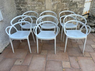 six chaises en plastique blanc disposées devant un mur de pierre