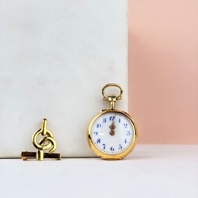 une montre de poche en or posée à côté d'une clé sur un bloc de marbre