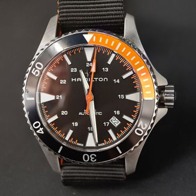 une montre noire avec une trotteuse orange sur fond noir