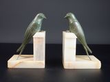 une paire d'oiseaux verts posés sur des serre-livres en marbre, sur fond noir