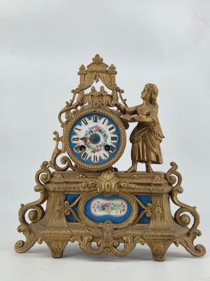a clock that is sitting on a table with a statue on top of it
